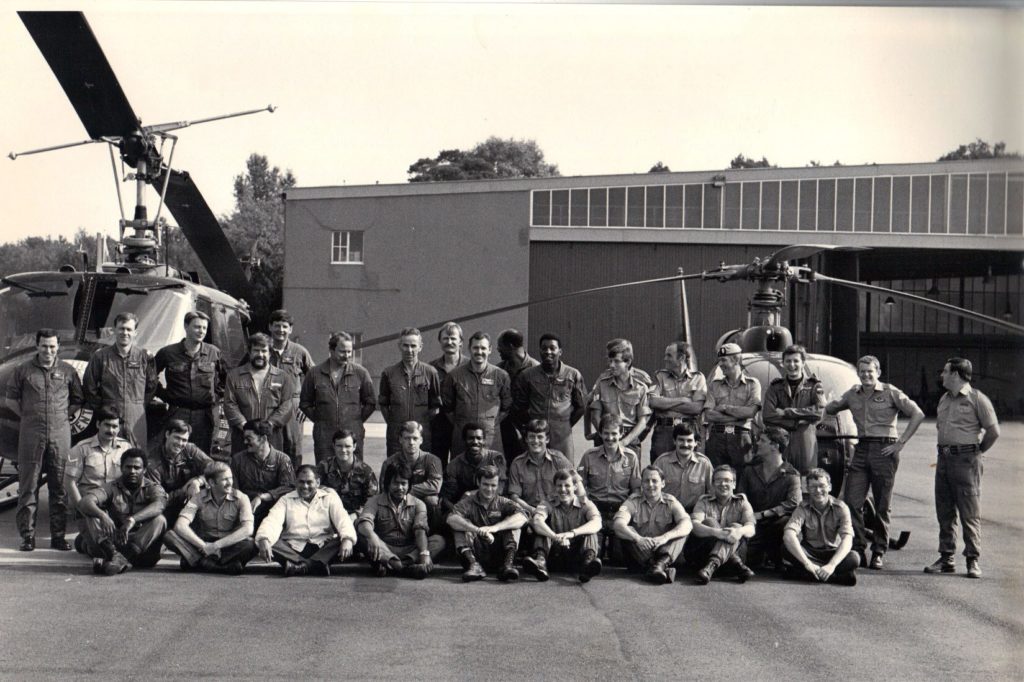 A black and white photo showing a group of US and British army personnel pose in front of two helicopters.