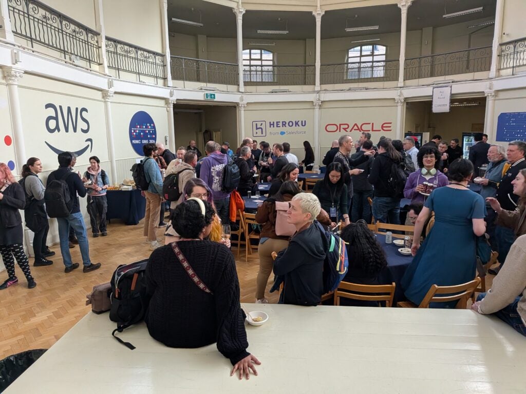 the secondary auditorium, a bunch of lovely people in a Victorian building, with sponsor logos for AWS, Heroku, and AWS on the walls.