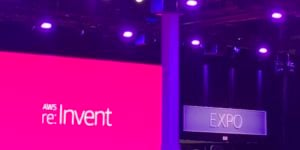 A sign that reads "Expo" is displayed above a door. To the left is a screen projecting text that reads "AWS re:Invent"