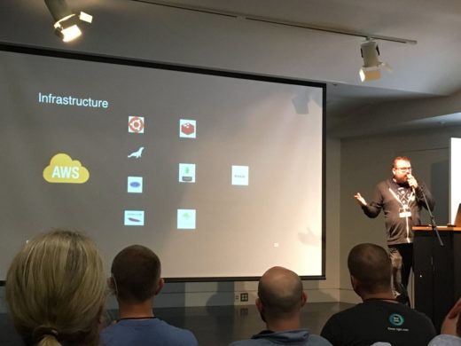 Greg Avola on stage with logos of their infrastructure stack.