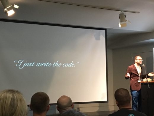 Kevin Barrett on stage with a slide stating I just write the code.