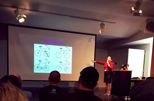 Cici Correa on stage with a slide showing attempts at drawing bikes from memory.