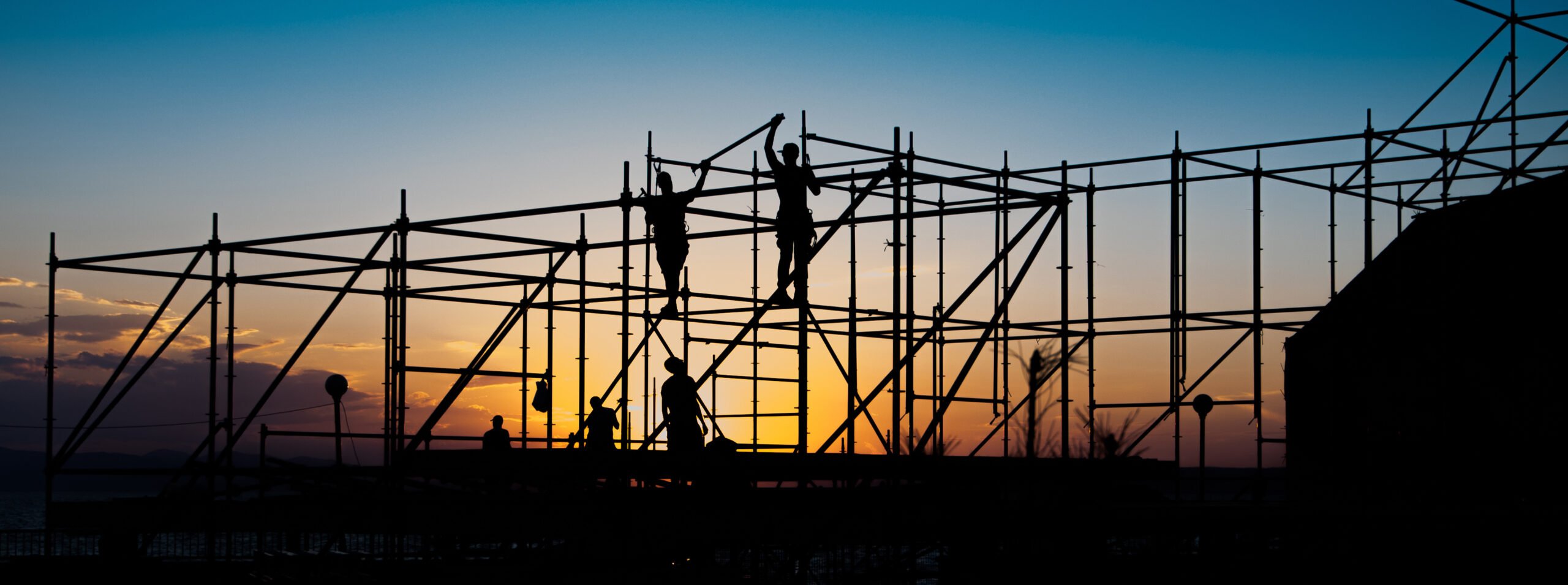 Silhouettes of workers building scaffolding at sunset